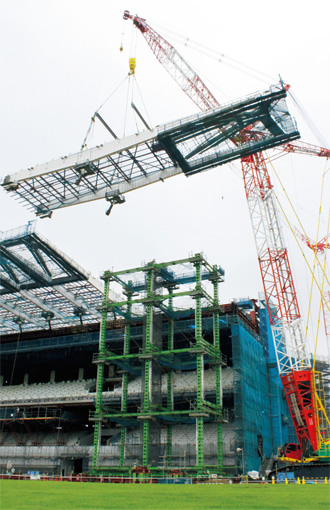 写真：ベットネット スポーツ鉄骨上架作業の様子。長さ37m・幅8m・重さ75tのベットネット スポーツ鉄骨が天空高く吊りあがった