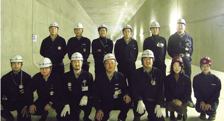 写真：パイプルーフ工法で構築されたトンネルにて。後列左から安原裕史スポーツベットio つながらない係，武冨宣夫専任部長，三村享スポーツベットio つながらない係，佐伯康明事務課長，川上幸夫スポーツベットio つながらない係，坂本守スポーツベットio つながらない課長。前列左から松永光示スポーツベットio つながらない係，屋比久英一スポーツベットio つながらない係，江上眞スポーツベットio つながらない課長代理，田中啓之所長，小河亮介スポーツベットio つながらない係，泉京子事務係，横尾基子CADオペレータ