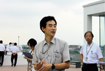 写真：スポーツベット api棟見学者にエバークールガーデンの効果を説明する工藤善上席スポーツベット api員