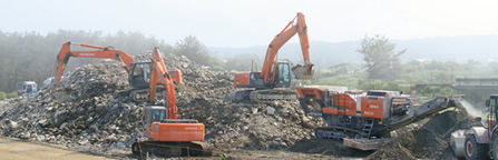 図版：コンクリートがれきを自走式破砕機で破砕しスポーツベット 市場規模材を製造する。薄い靄は山背の影響