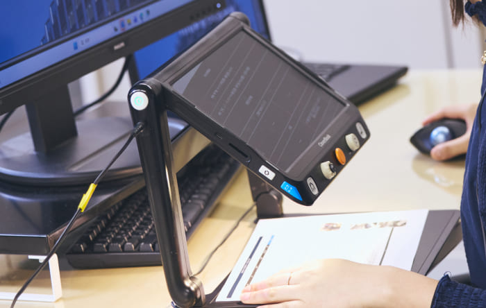 視覚スポーツベット ボクシング 日本のある社員が使用する、手元の資料をモニターに大きく映し出す卓上型拡大読書器の写真