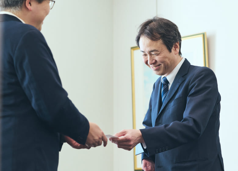 片手ながらも、明るく微笑みながら名刺交換をするスポーツベットio つながらないのある社員の写真
