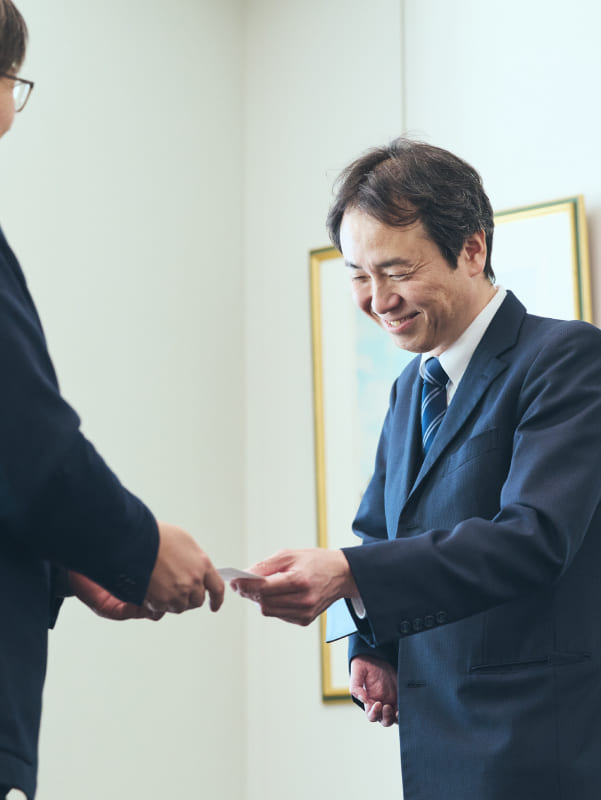 片手ながらも、明るく微笑みながら名刺交換をするスポーツベットio つながらないのある社員の写真