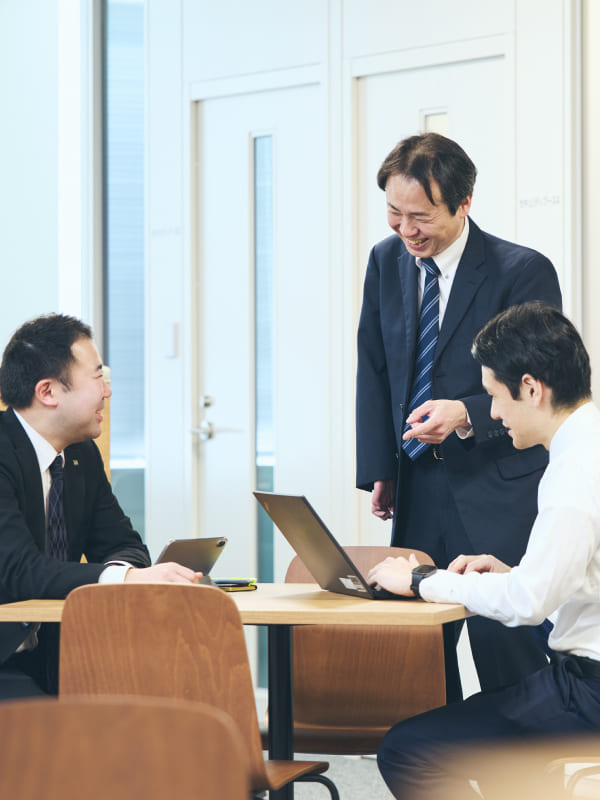 会議室で資料を囲んで打ち合わせをする右上肢スポーツベットio つながらないの男性社員と同僚たち。身振り手振りを交えてフランクに会話する業務風景の写真