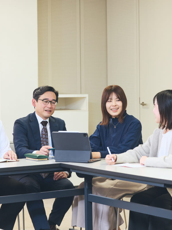 会議室でタブレット端末を囲み、チームメンバーと真剣な表情で意見を交わす女性社員の写真